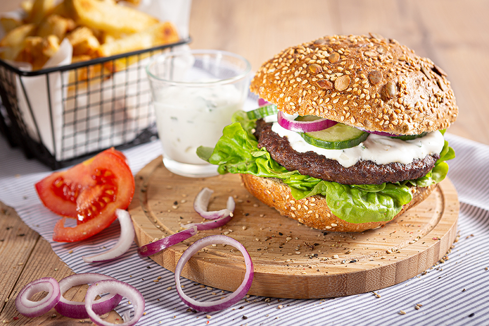 Nahaufnahme eines saftigen Burgers mit frischen Tomaten und roten Zwiebeln, dekorativ fotografiert.