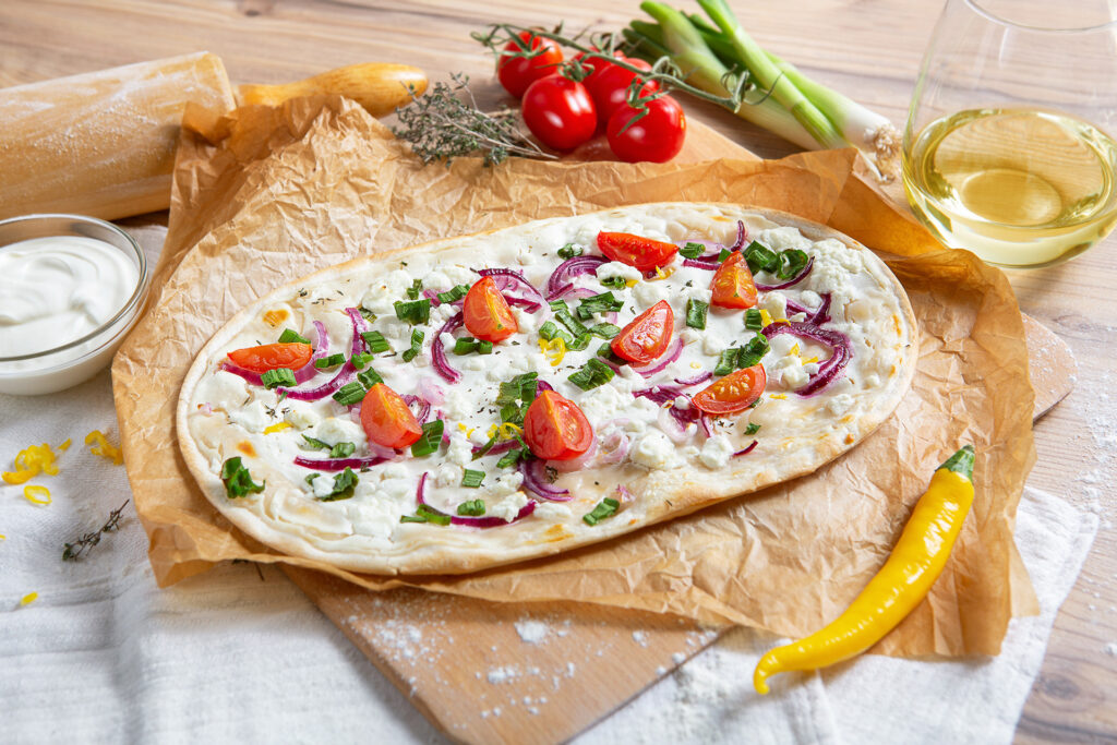Flammkuchen mit Gemüse auf Backpapier neben frischen Zutaten, bearbeitet für professionelle Produktpräsentation.